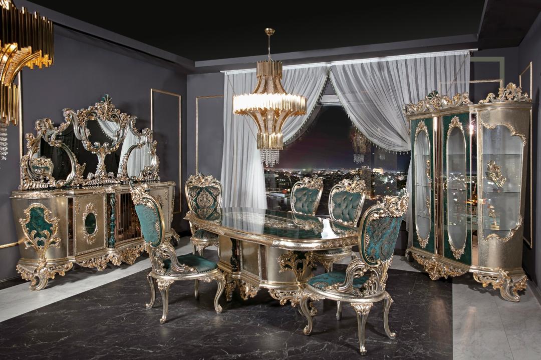 A luxurious dining room set featuring emerald green upholstery and gold or silver-leafed carvings, with a grand dining table and matching chairs.