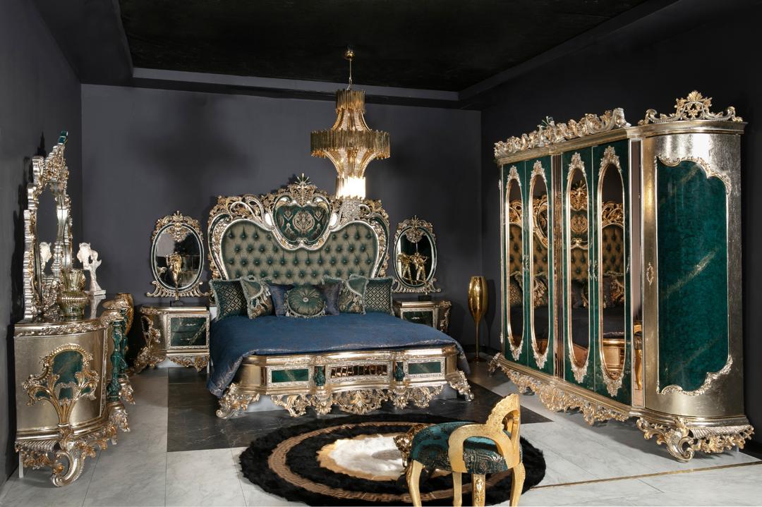 A luxurious bedroom set with emerald green upholstery and gold or silver-leafed carvings, including a bed with an ornate headboard and footboard, nightstands, and a dresser.